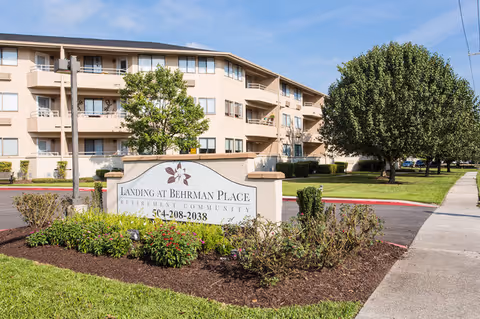 A multi-story beige senior living building with a landscaped entrance sign that reads Landing at Behrman Place.