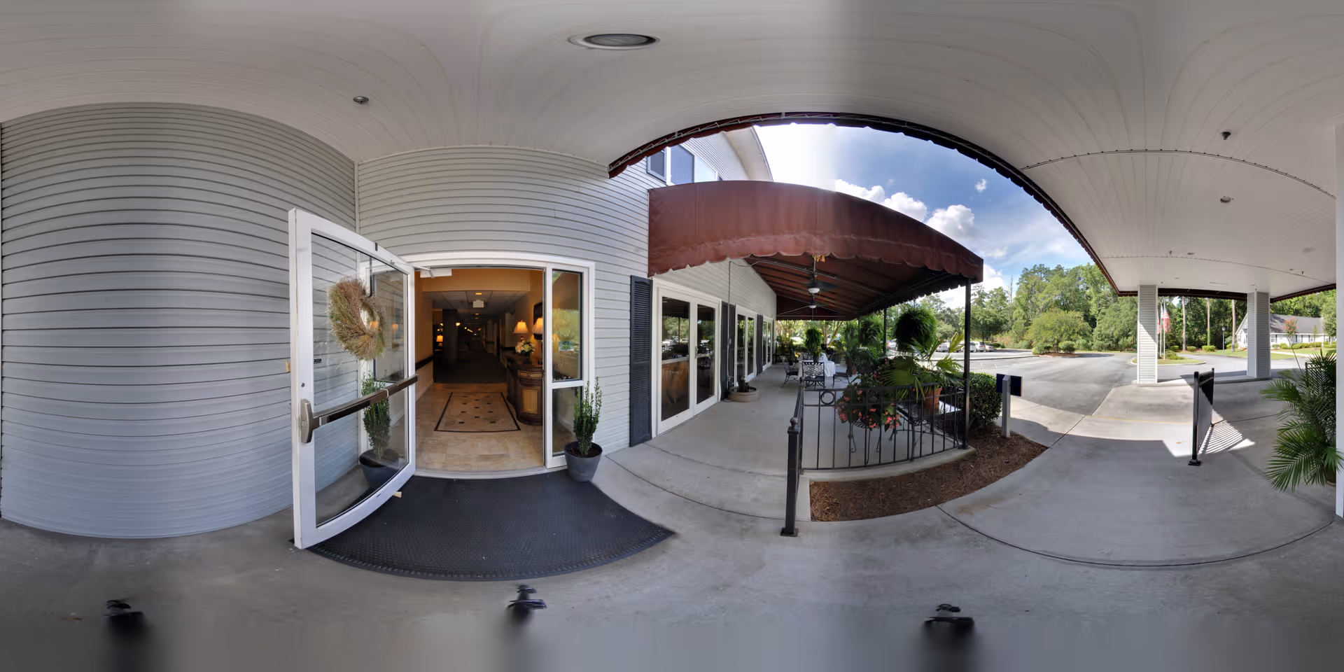 Covered front entrance and drop-off area with open glass doors, awning, potted plants, and seating.
