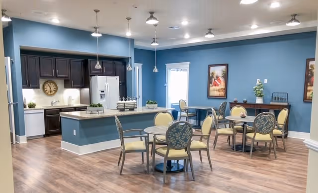 Communal dining area with round tables and chairs next to an open kitchen with blue walls and pendant lighting.