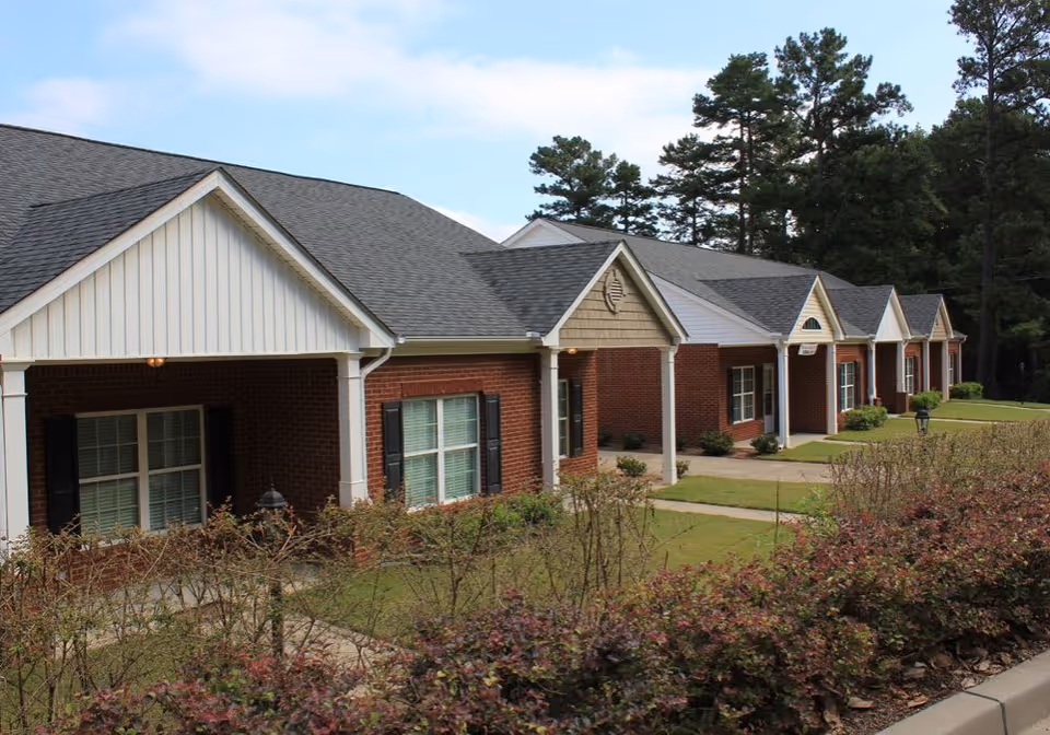 Single-story brick senior living units with covered porches, neatly trimmed lawns, and trees behind them.