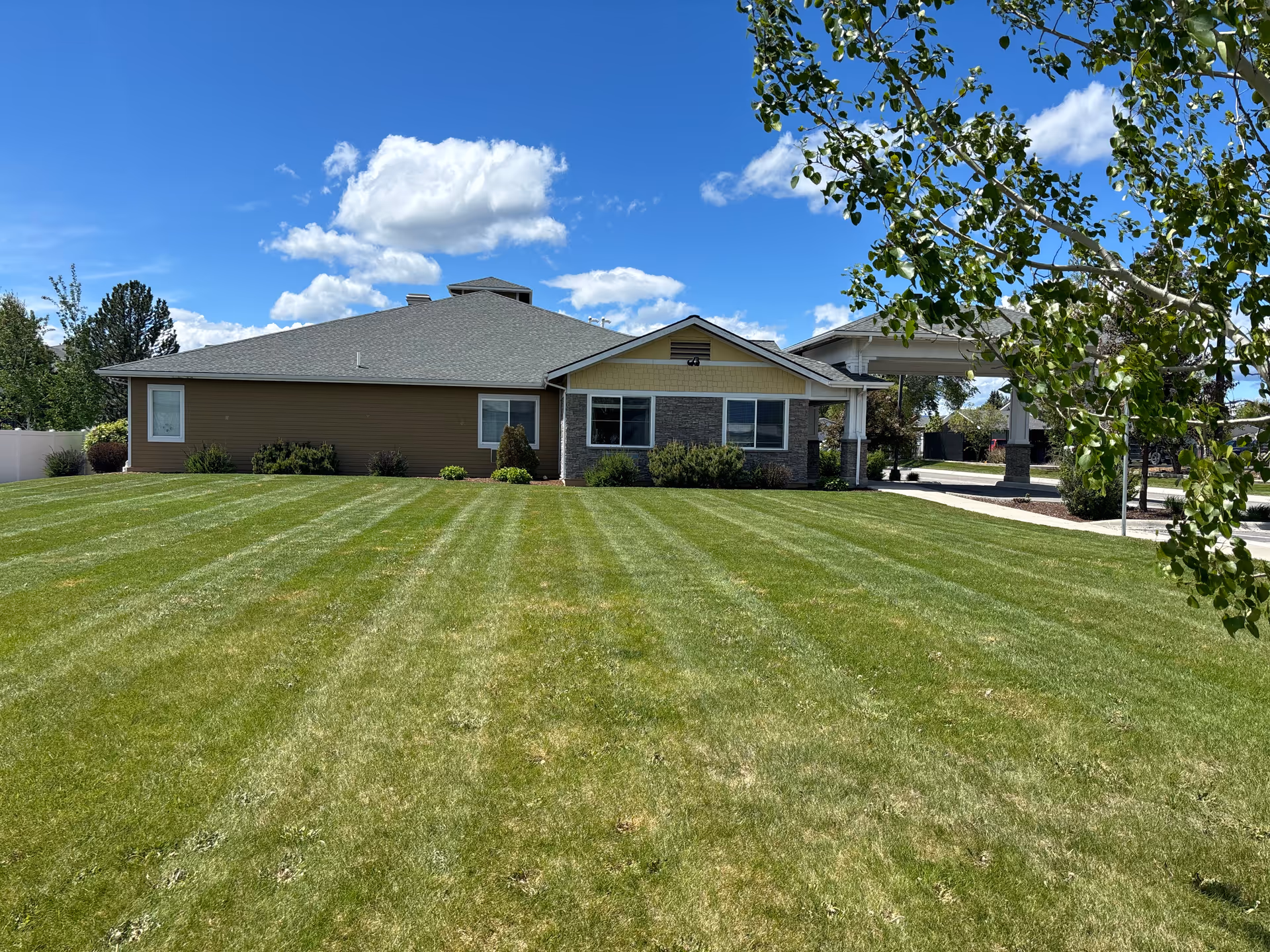 Front exterior of a single-story assisted living building with a wide striped lawn under a blue sky.