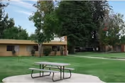 Outdoor scene with a picnic table on a circular pad near a beige senior facility.