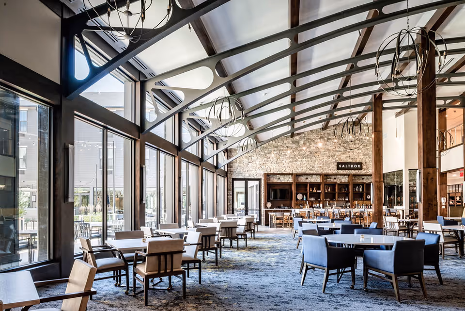 Spacious modern dining room with floor-to-ceiling windows, multiple tables and chairs, and a stone-backed service area labeled "SALTBOX."