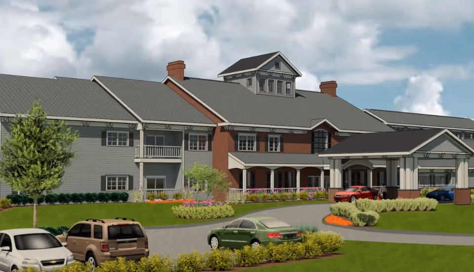 Exterior view of a senior living facility named Ciel of Princeton, showing a large building with a covered entrance, multiple windows, and a landscaped driveway with parked cars and greenery.
