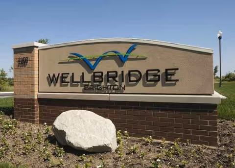 A WellBridge Brighton sign on a brick base, with landscaping.