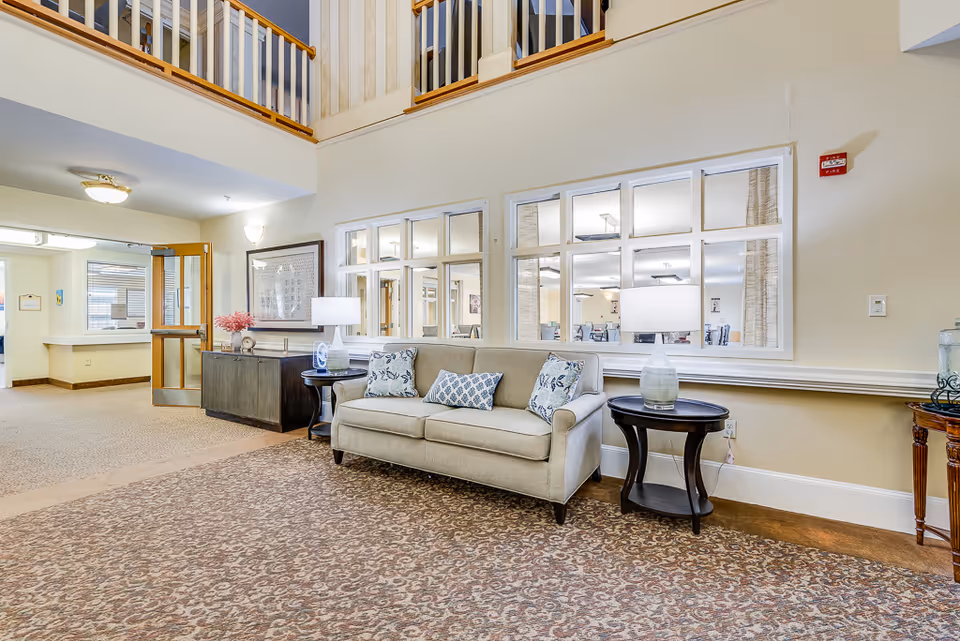 Lobby seating area with a beige sofa, patterned cushions, side tables and lamps in a senior living facility.