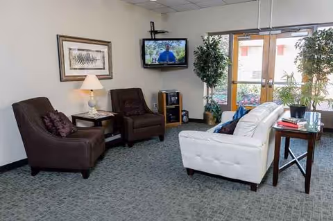 Lounge area with white sofa, brown chairs, TV, art, plants, and glass doors.
