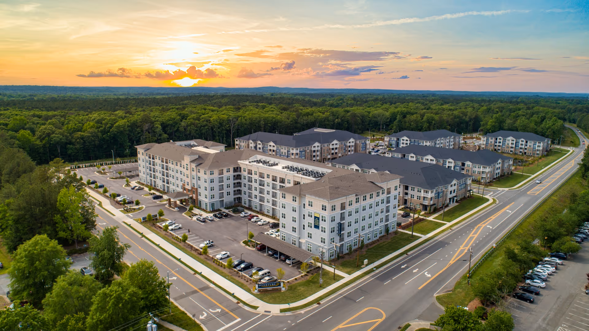 Aerial view of a large multi-building senior living community surrounded by trees at sunset.