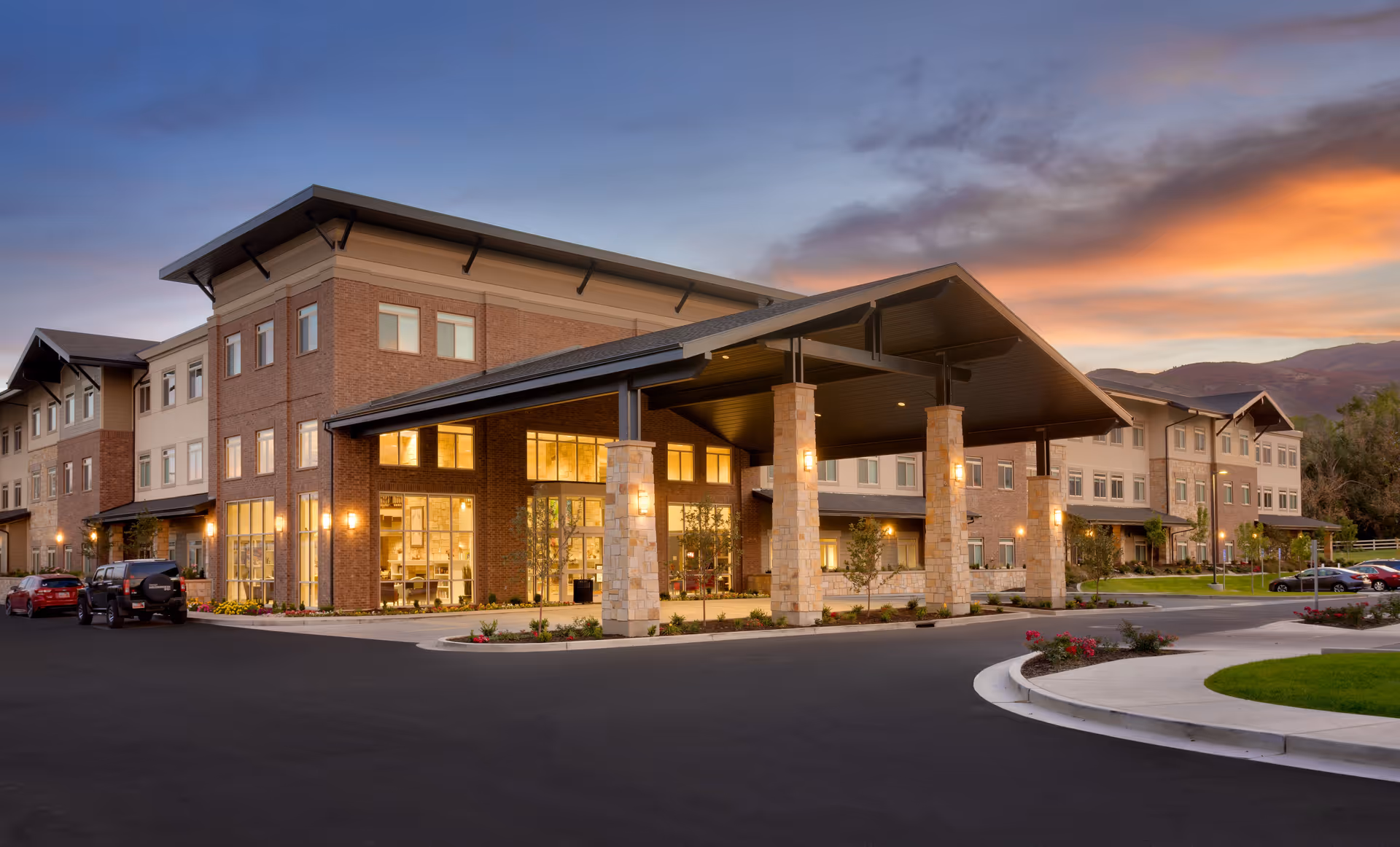 Front exterior of a three-story senior living building with a large covered entrance at sunset.
