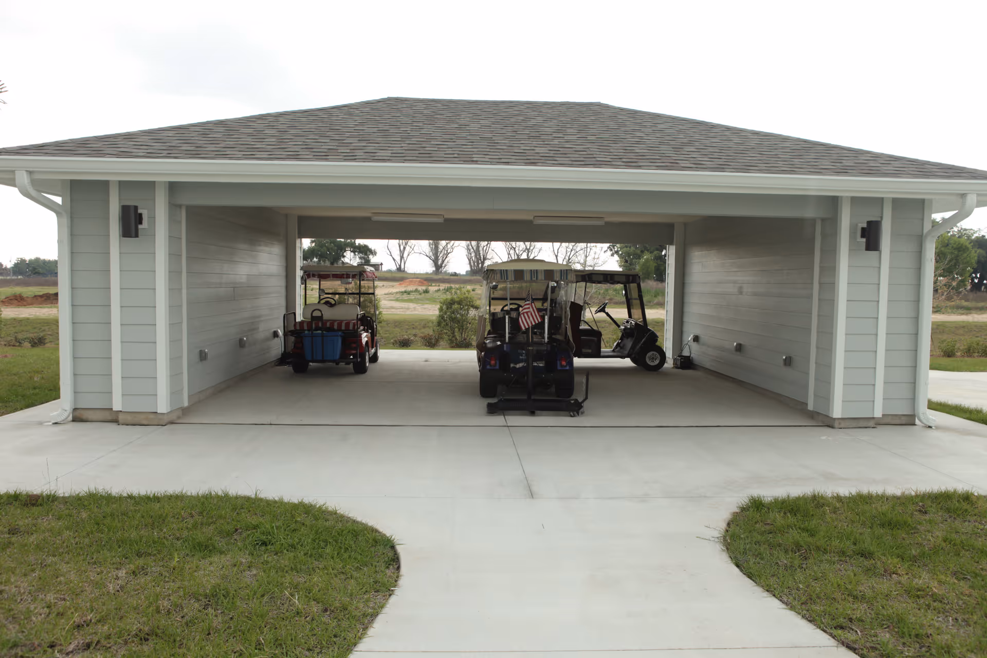 Covered parking area with three golf carts parked inside, surrounded by grass and open land in the background.