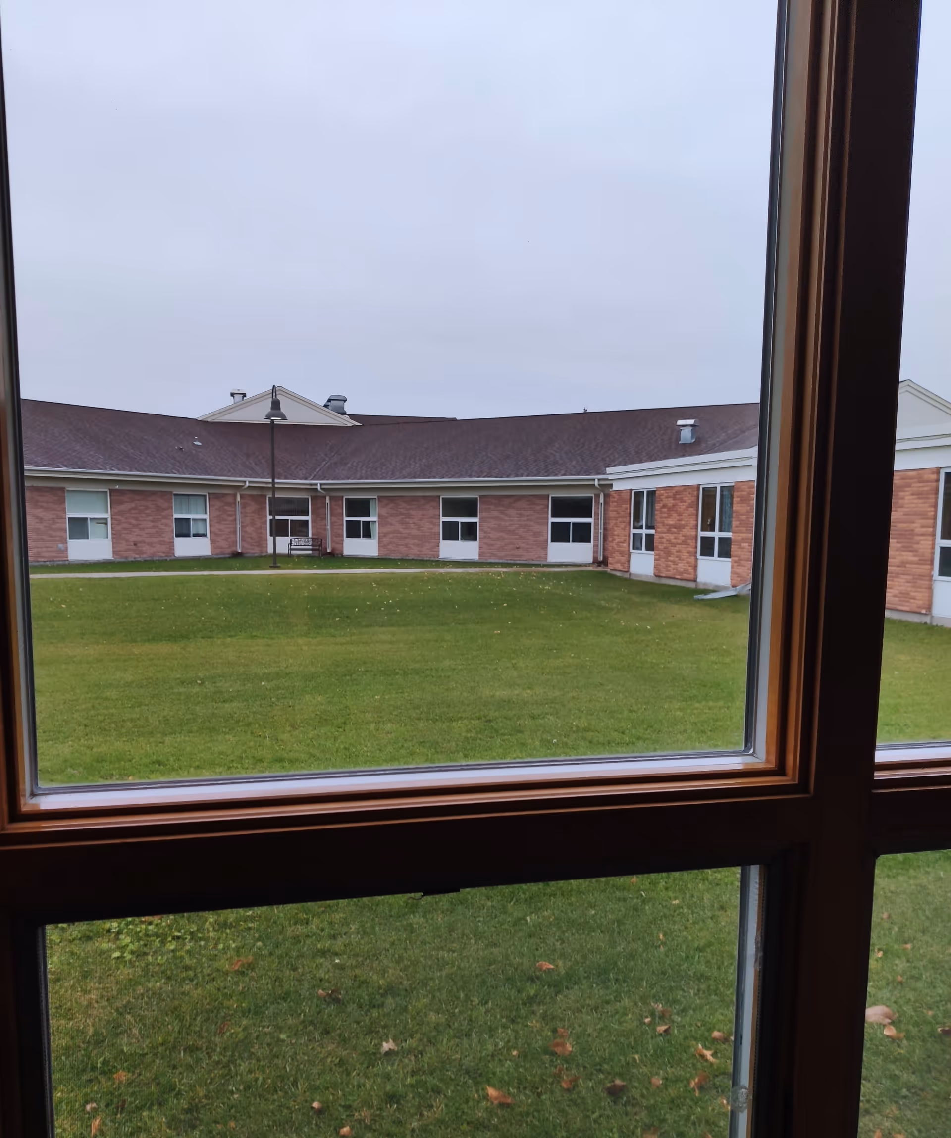 View through a window of a grassy courtyard surrounded by a single-story brick building.
