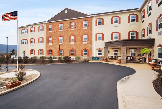 Exterior view of Leighton Place featuring a brick facade, entrance area with seating, and landscaped surroundings.