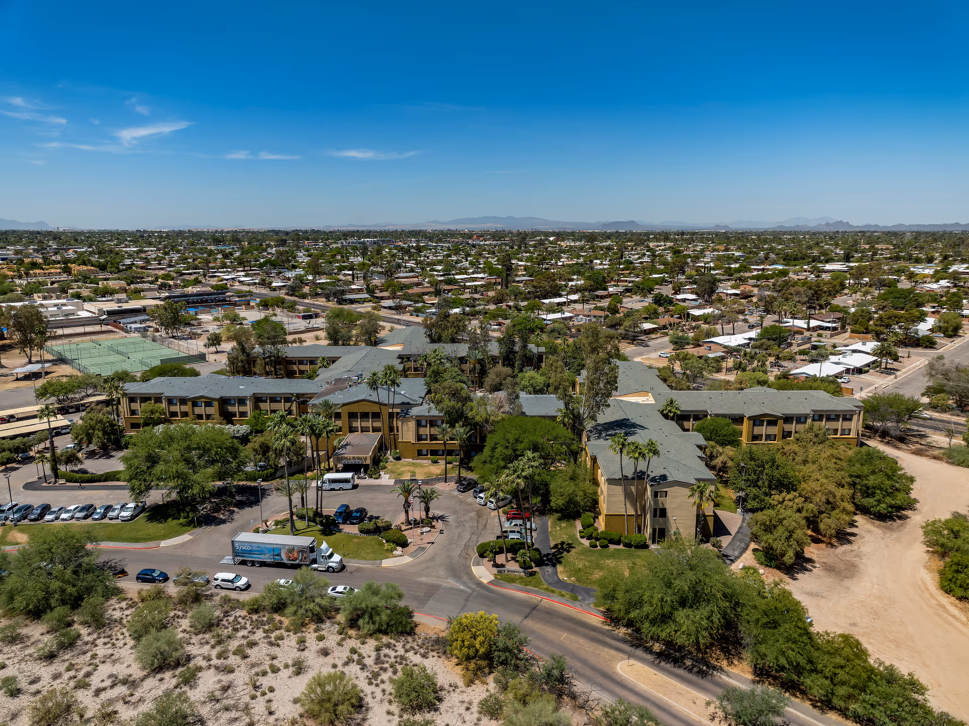 Aerial view of the Broadway Proper Assisted & Senior Living complex with parking, surrounding trees, and nearby residential neighborhood.