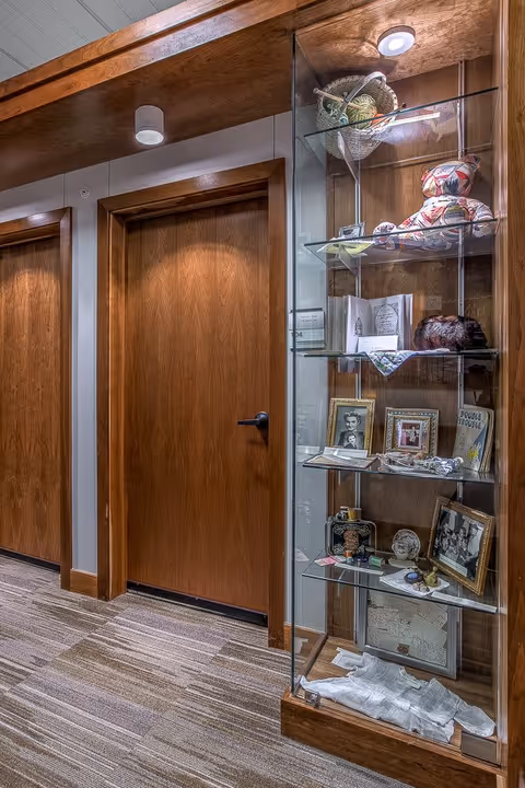 Indoor hallway with wooden doors and a glass display case holding framed photos and memorabilia.