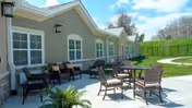 Outdoor patio area at The Reserve at Spring Hill featuring several chairs and tables on a concrete surface next to a building with multiple windows and a grassy hill in the background under a partly cloudy sky.