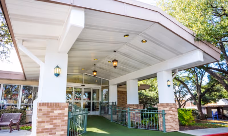 Covered entrance/portico of the assisted living facility with brick columns, hanging lantern lights, and glass doors.