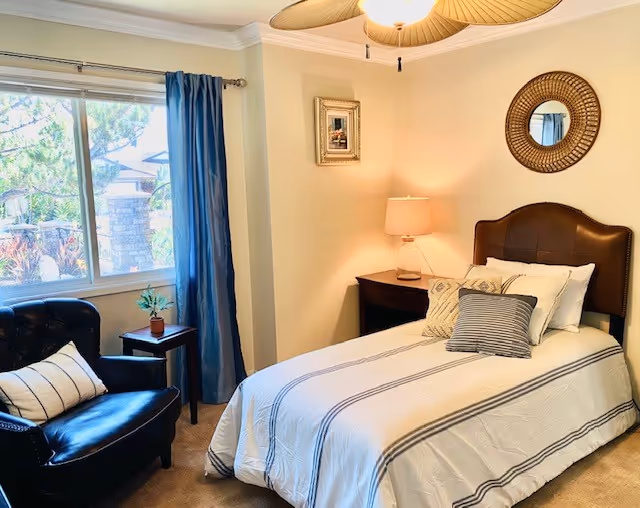 Cozy bedroom in a senior living facility with bed, nightstand, lamp, and window