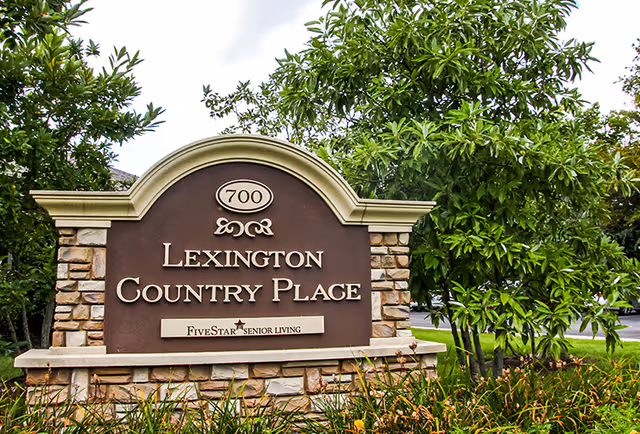 Stone and brick sign for Lexington Country Place senior living community with the address number 700, surrounded by greenery and trees.