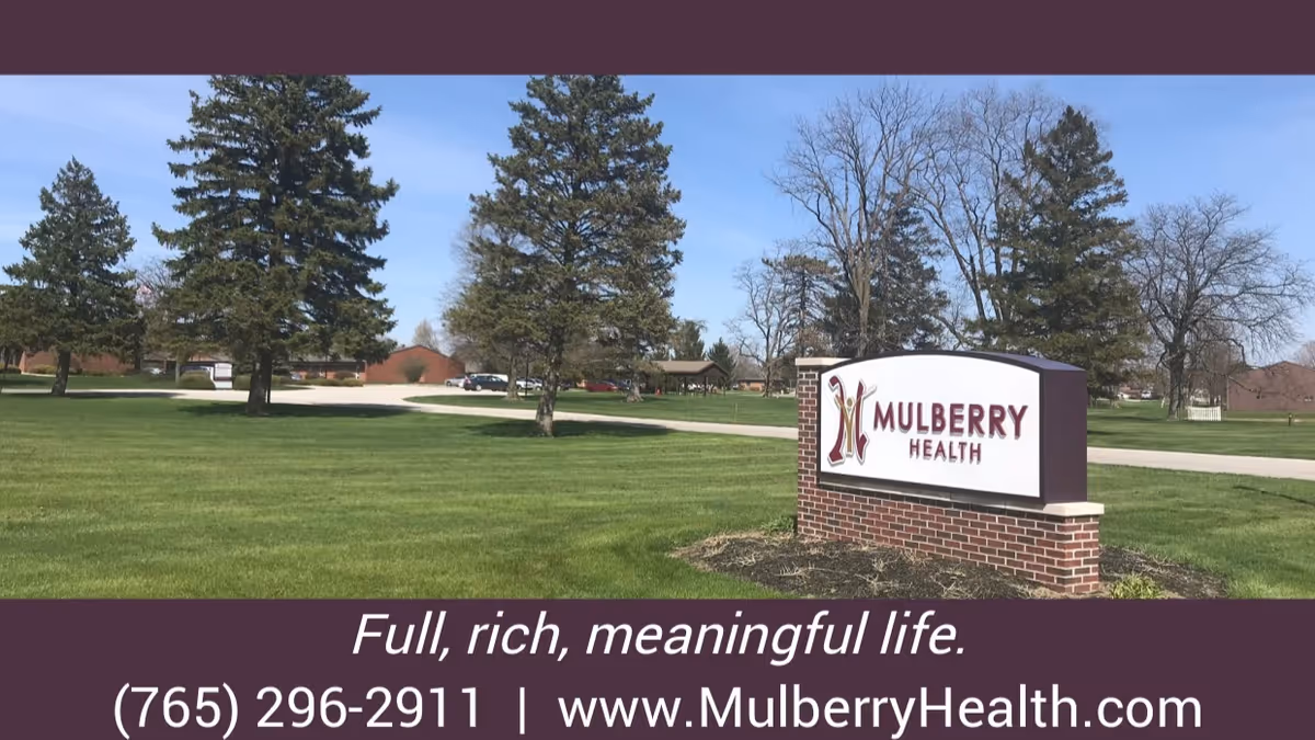 A landscaped lawn and trees with a brick sign that reads "Mulberry Health" and a promotional banner showing a phone number and website.