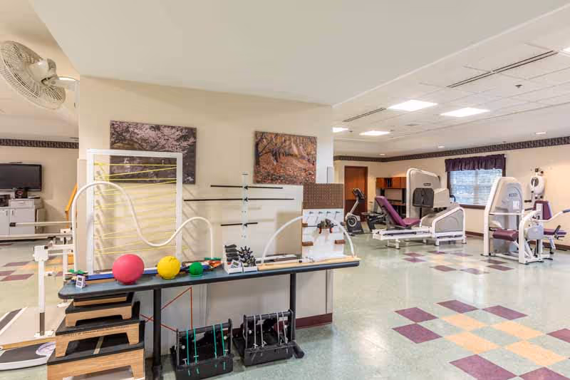 Spacious rehabilitation gym with exercise machines, therapy equipment, balance rails, and colorful tiled floor.
