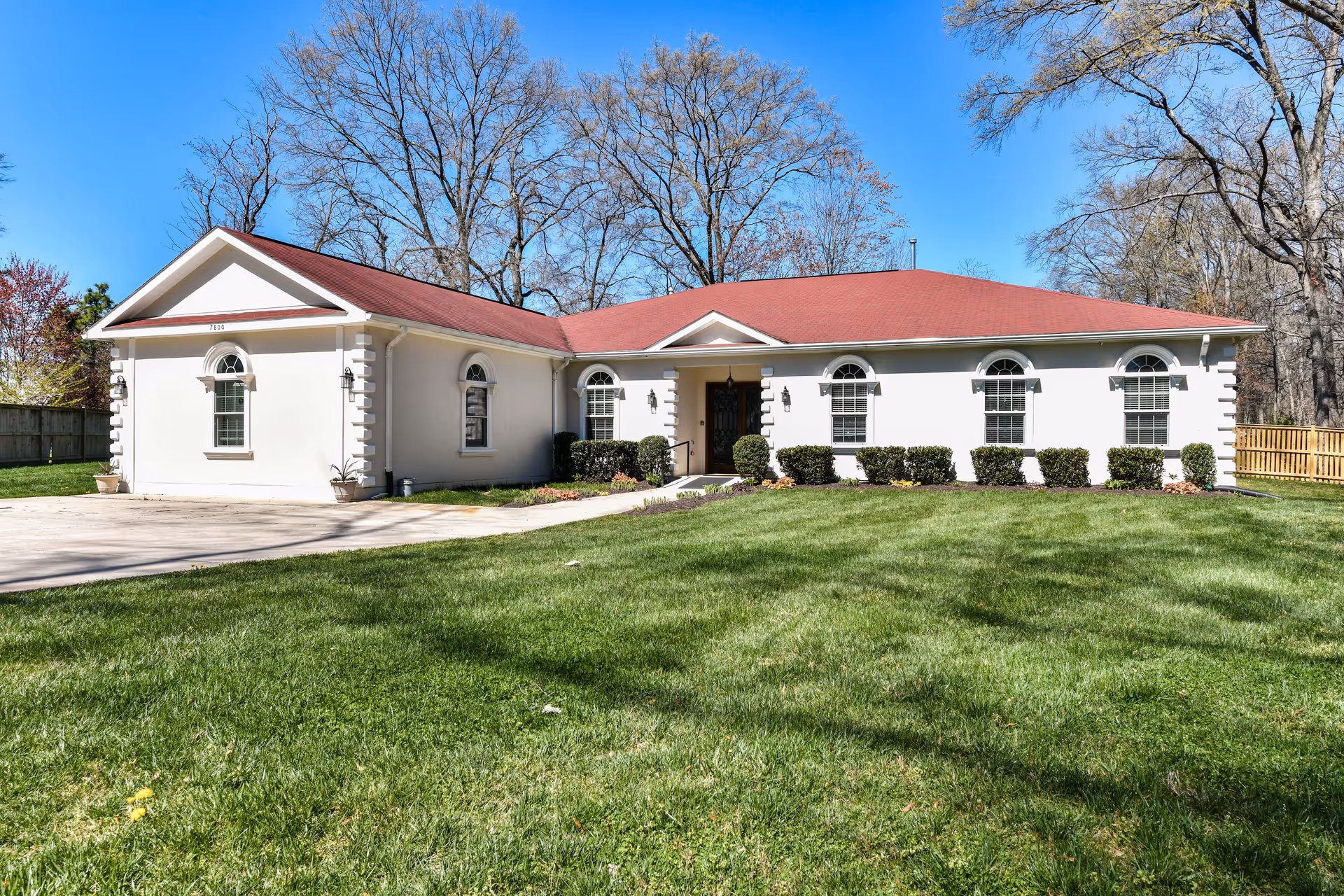 Single story memory care facility with white walls, red roof, and a well kept lawn.