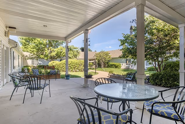 Covered outdoor patio with round glass-top tables and metal chairs overlooking a landscaped courtyard.