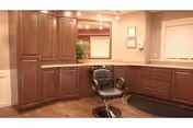 A wood-paneled grooming or salon room with a black swivel styling chair in front of a mirror and built-in cabinets and drawers.