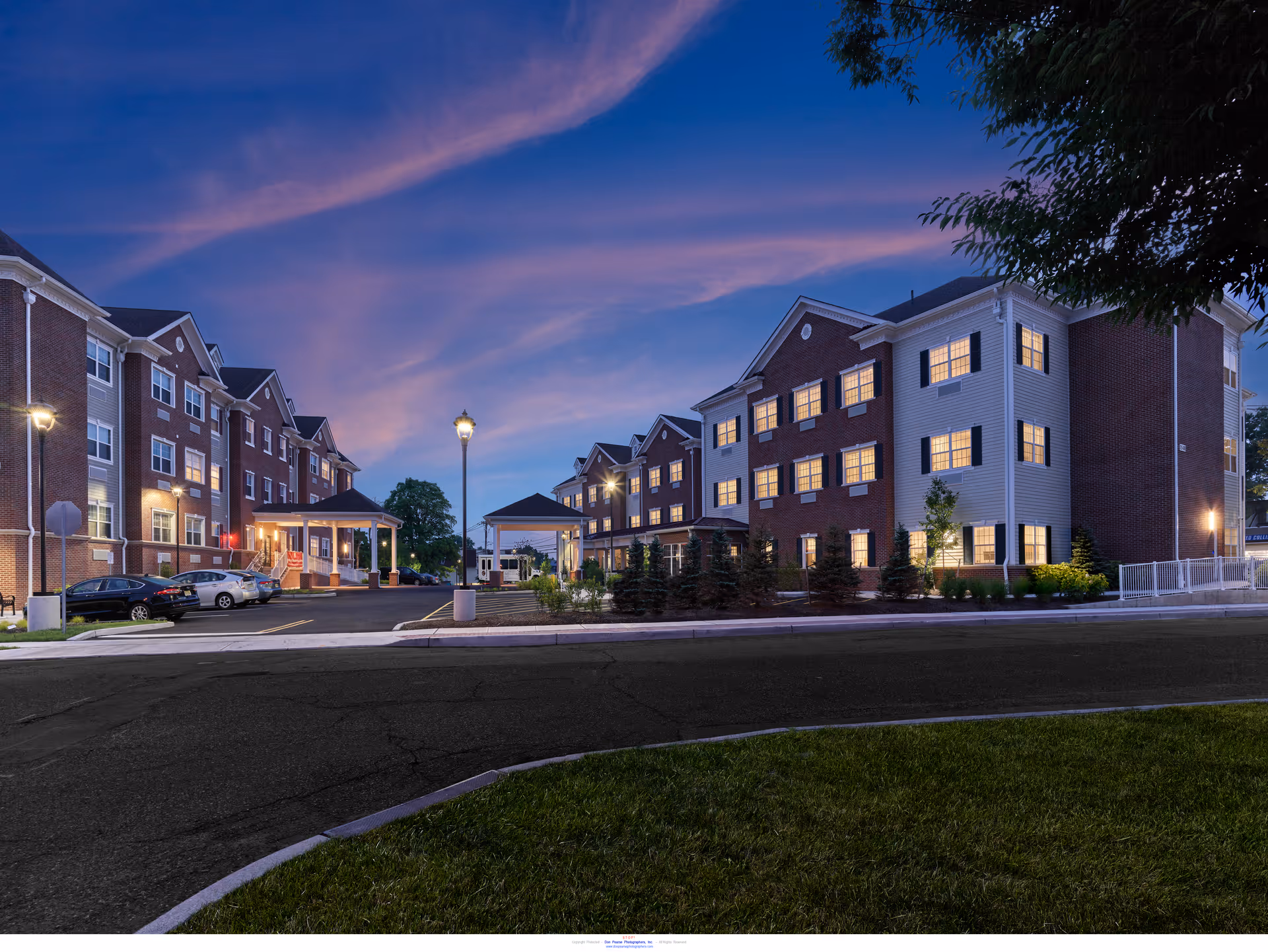 Evening exterior view of a multi-story brick senior living building with lit windows and a covered entrance.