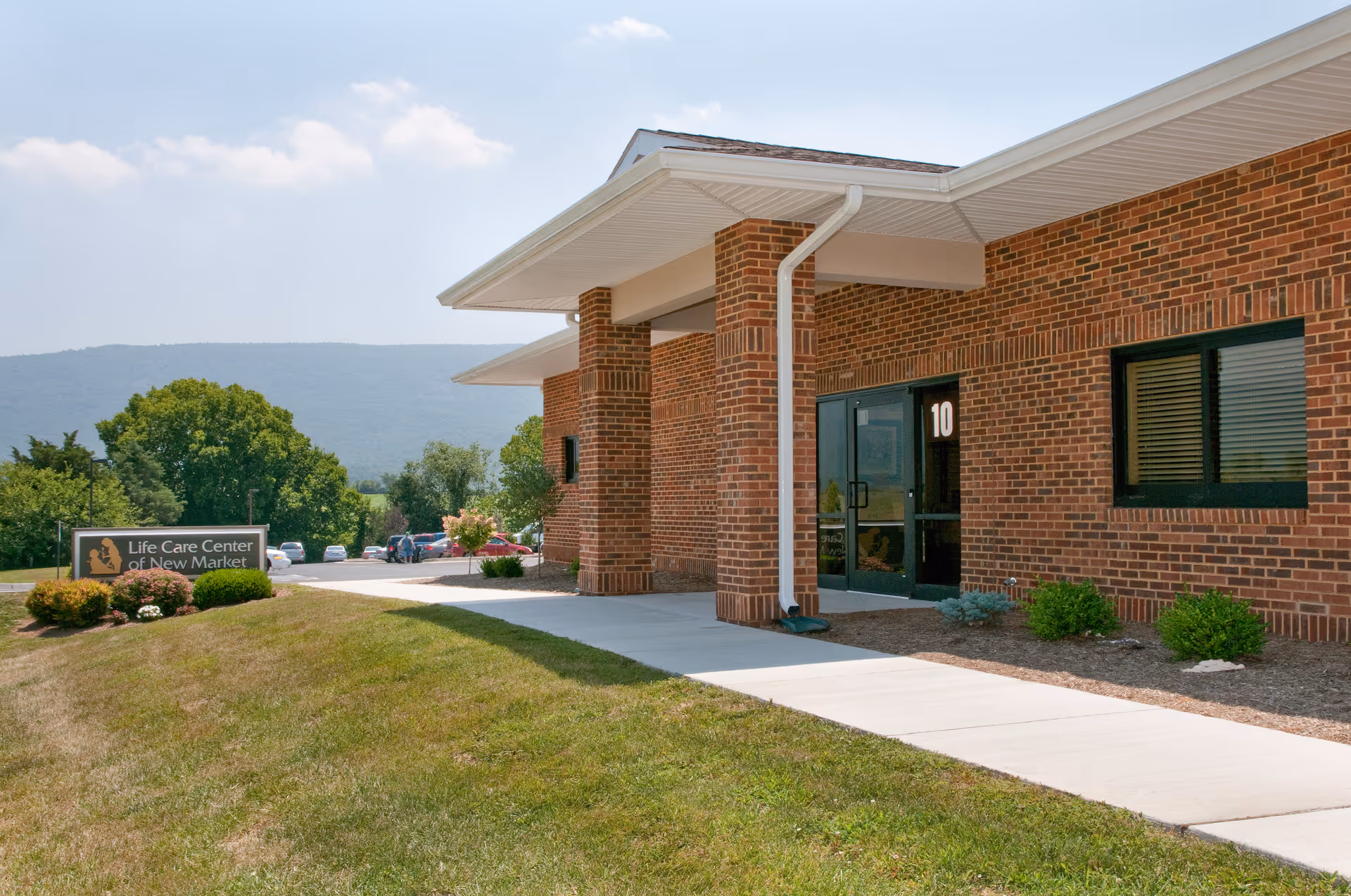 Front entrance of the Life Care Center of New Market showing a brick facade, covered walkway, and lawn sign.