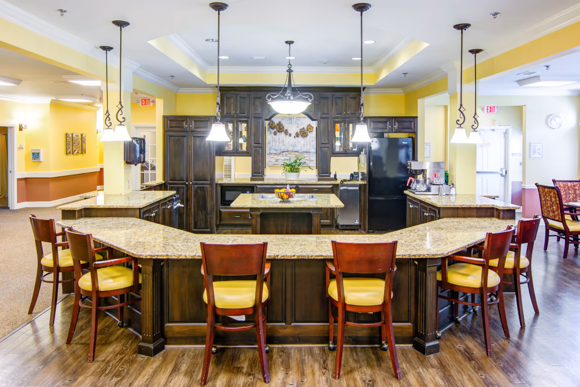 Communal kitchen area with a large granite island surrounded by wooden barstools and pendant lighting.
