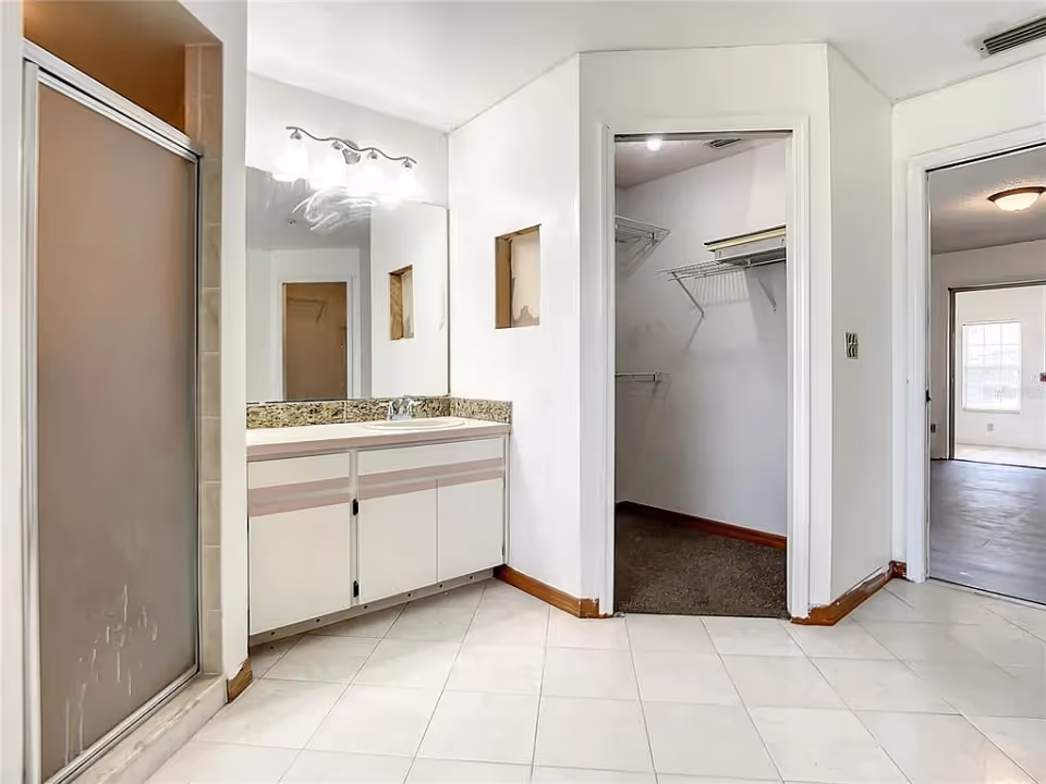 Bathroom with a single-sink vanity and mirror, a shower stall on the left, and an open walk-in closet and doorway to another room.