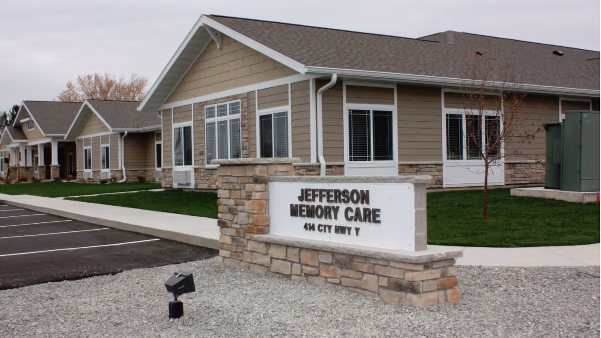 Single-story memory care building with a stone sign reading "Jefferson Memory Care" in front, parking area and lawn visible.