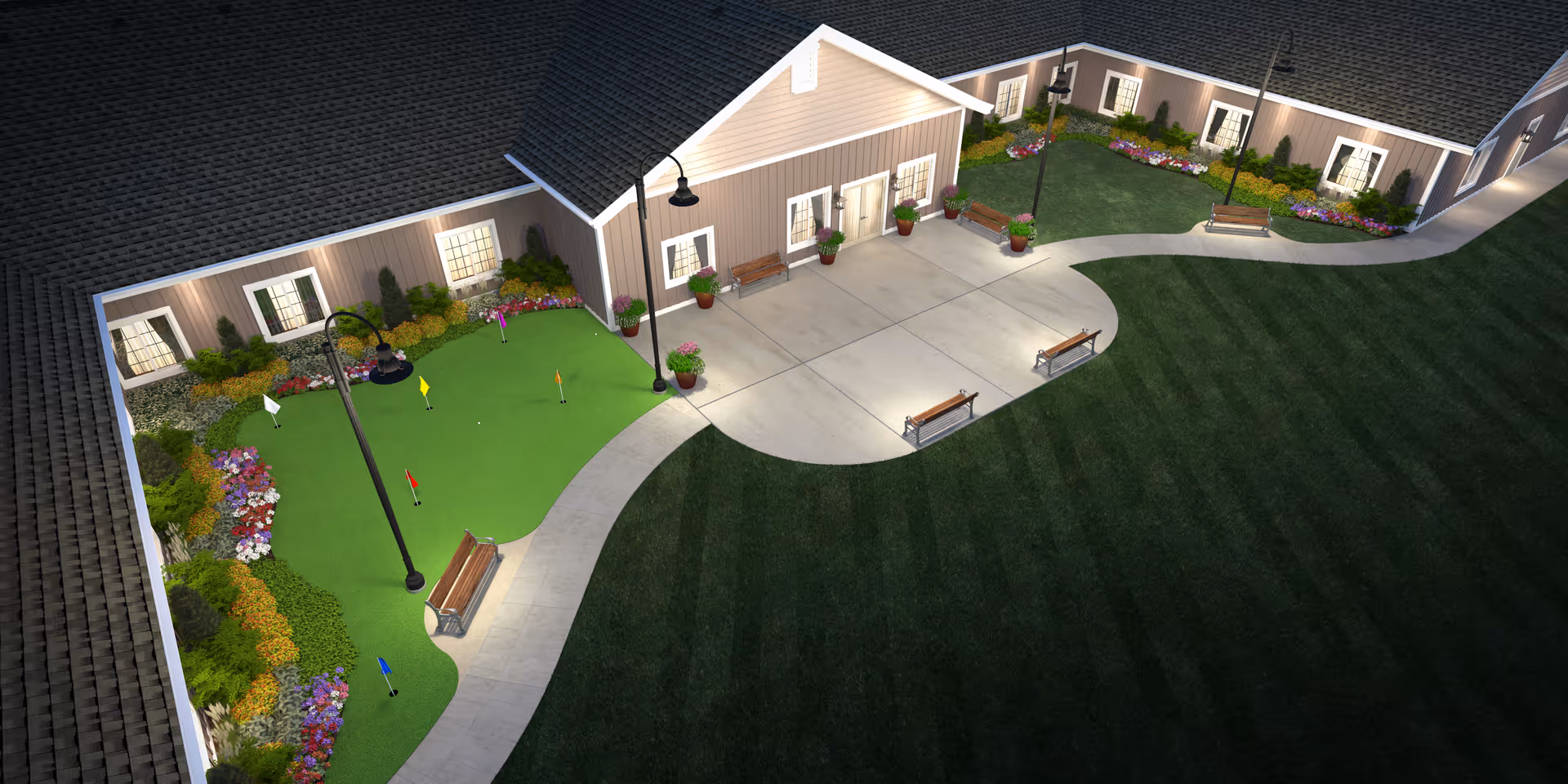 A nighttime aerial view of an outdoor courtyard area at The Legacy Assisted Living, featuring a small putting green with colorful flags, benches along a curved concrete pathway, flower beds, and exterior building walls with windows and doors illuminated by outdoor lamps.
