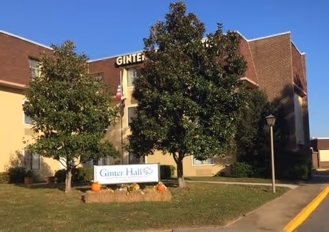 Exterior view of Ginter Hall South building with a sign in front surrounded by trees and pumpkins on the grass near the sidewalk.