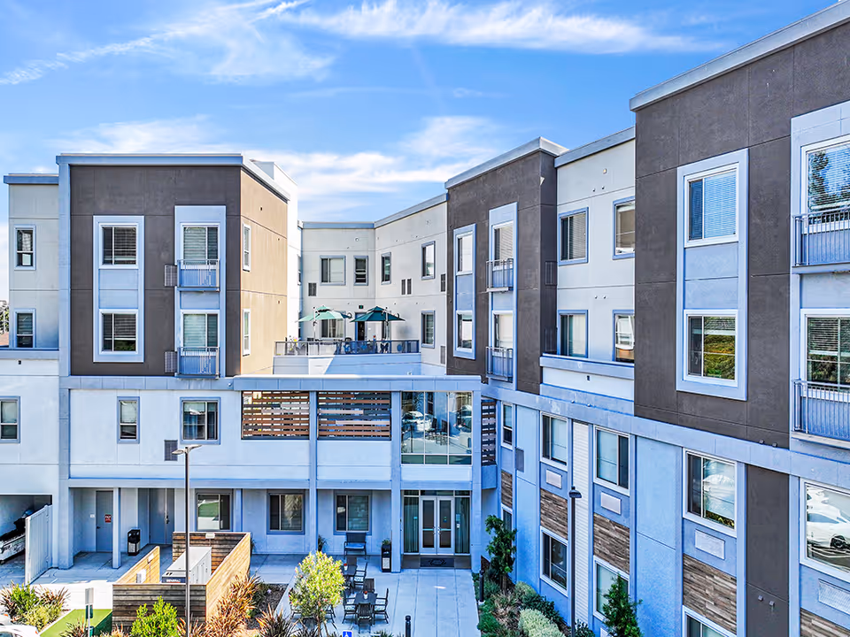 Exterior view of a modern multi-story senior living building with a central courtyard and outdoor seating.