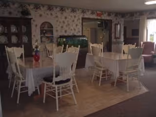 A dining room with white chairs around round tables and floral wallpaper.