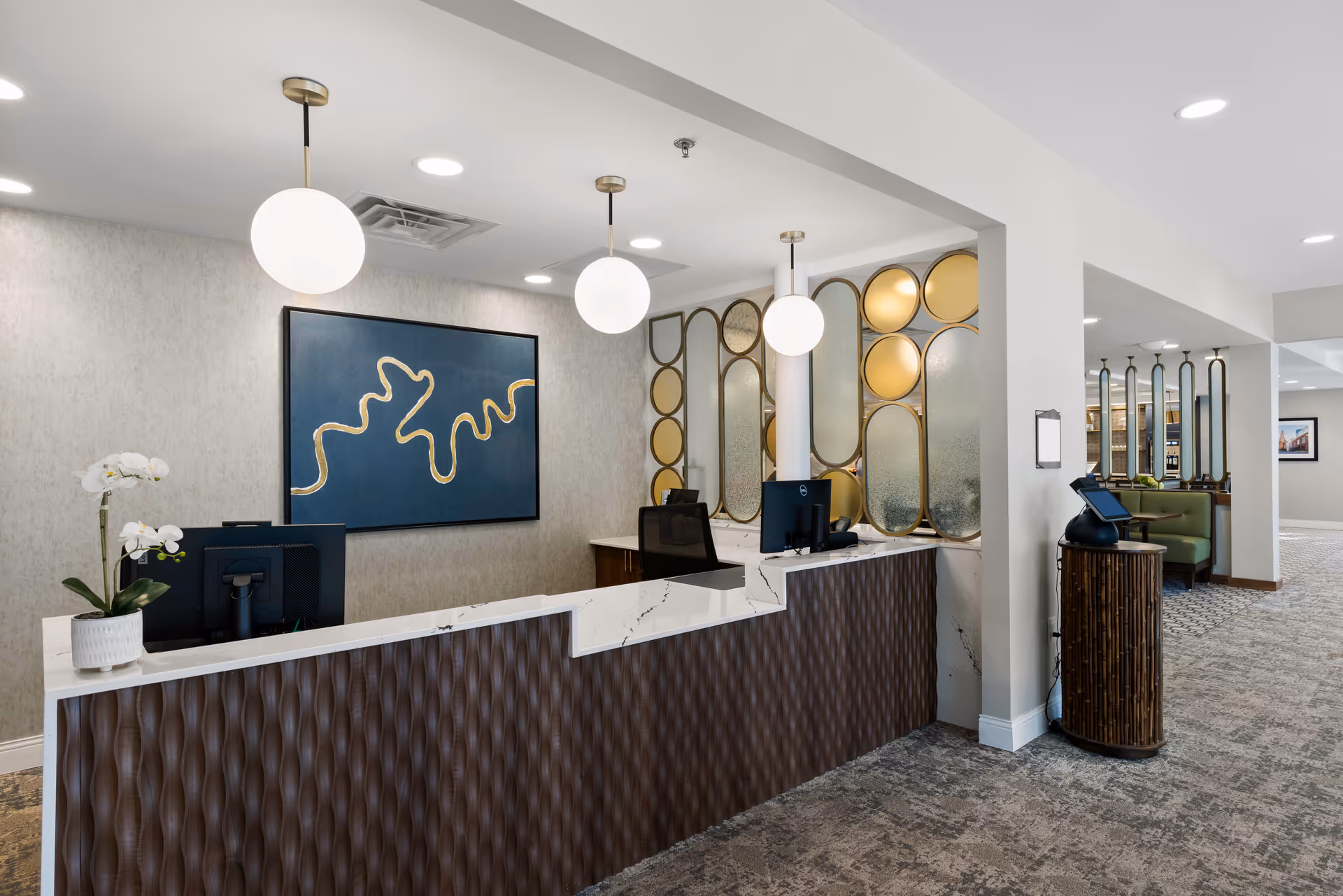 Reception desk and lobby area with pendant lights, decorative wall panels, computers, and seating in a senior living facility.