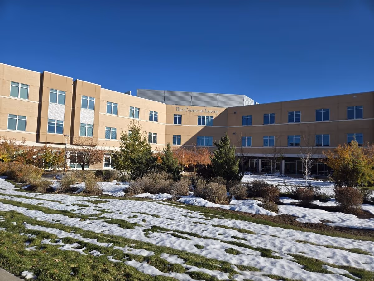 Front exterior of a three-story care facility building with a snowy lawn and clear blue sky.
