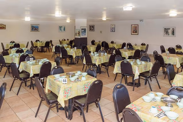 Large dining room with rows of small tables covered in yellow tablecloths, each set with dishes, utensils and table numbers.