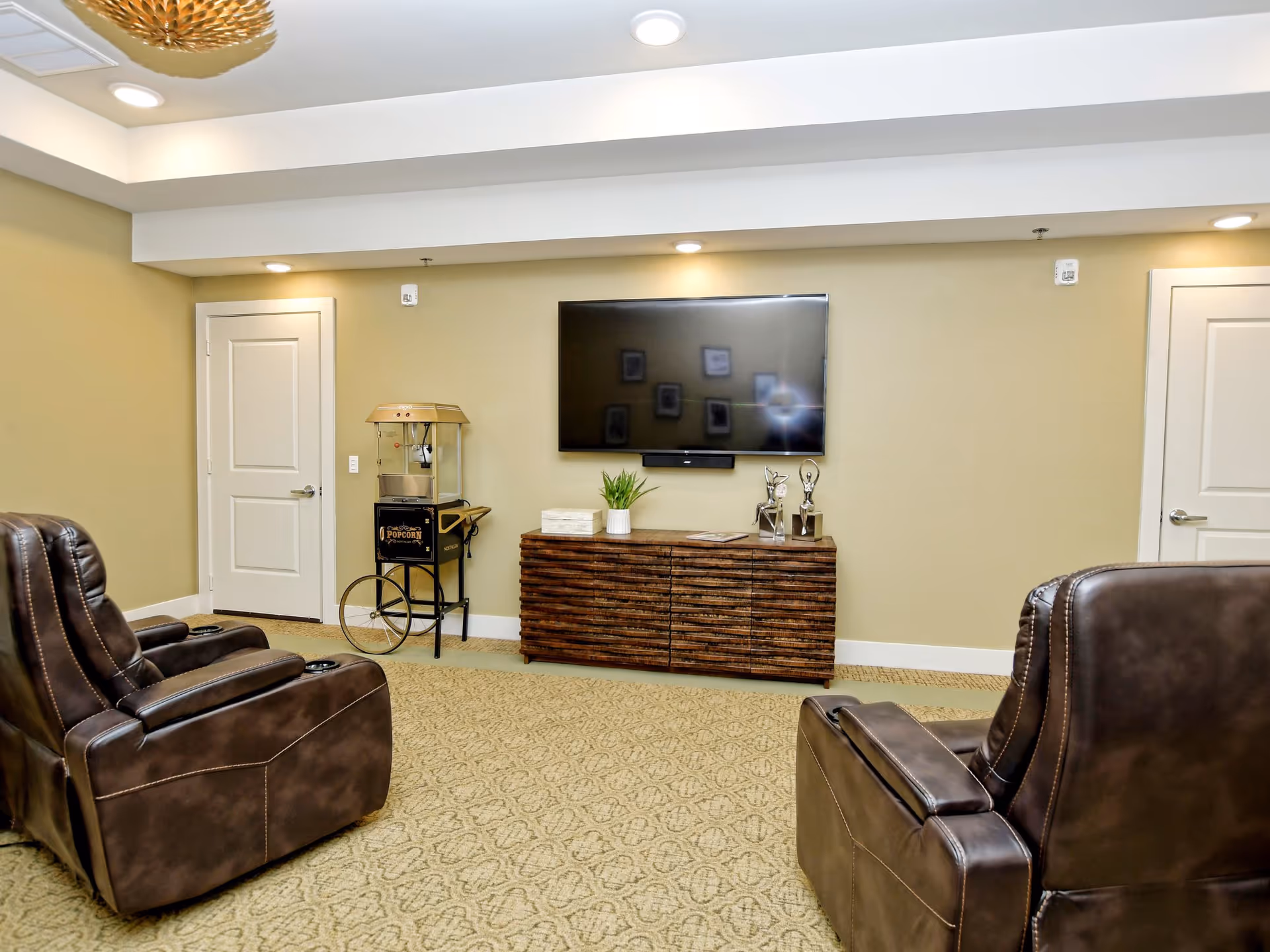 A cozy lounge with leather recliners facing a wall-mounted TV above a wooden console and a vintage popcorn cart.