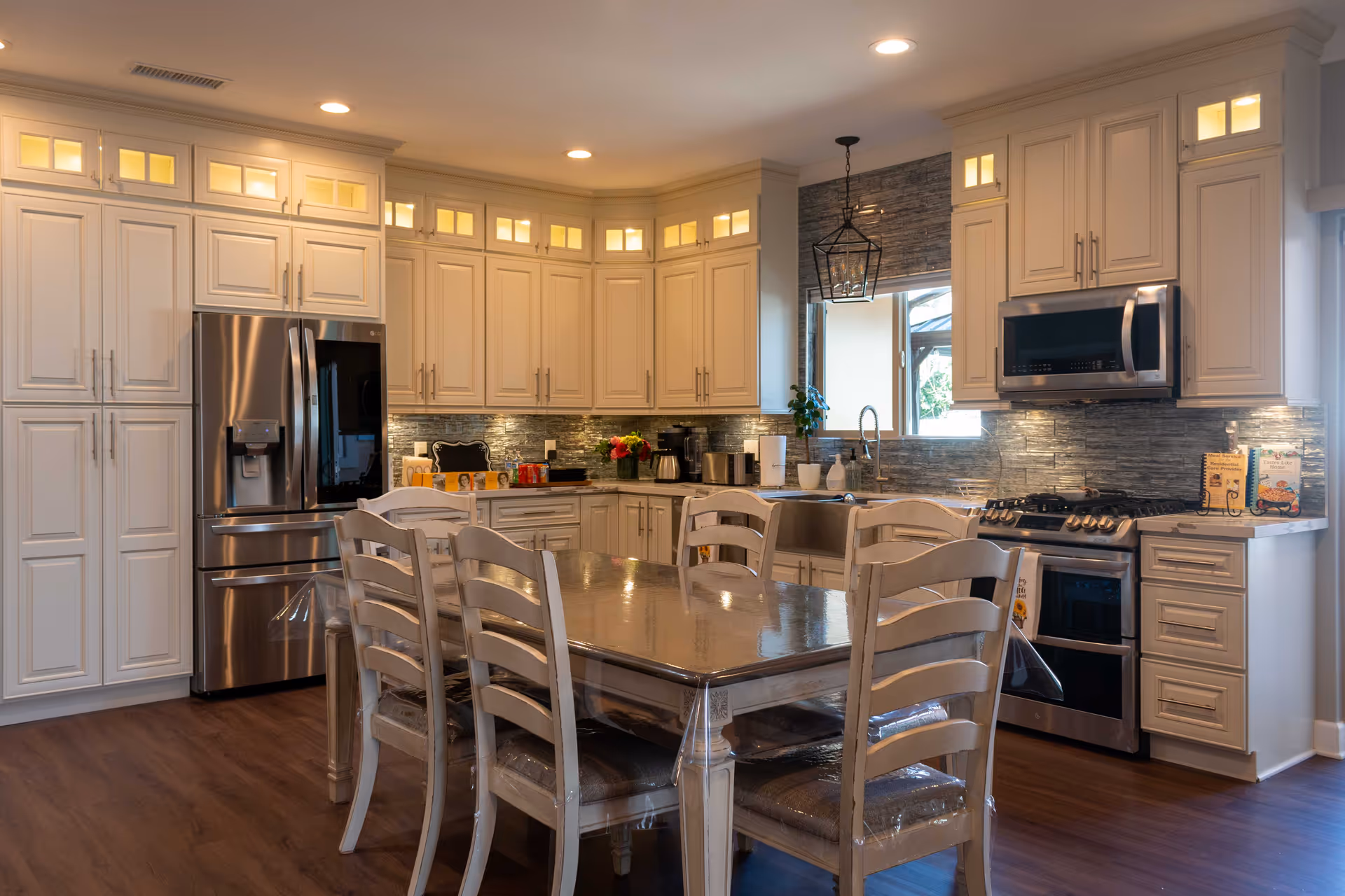 Spacious modern kitchen with a wooden dining table and chairs, white cabinets, stainless steel appliances, and pendant lighting.