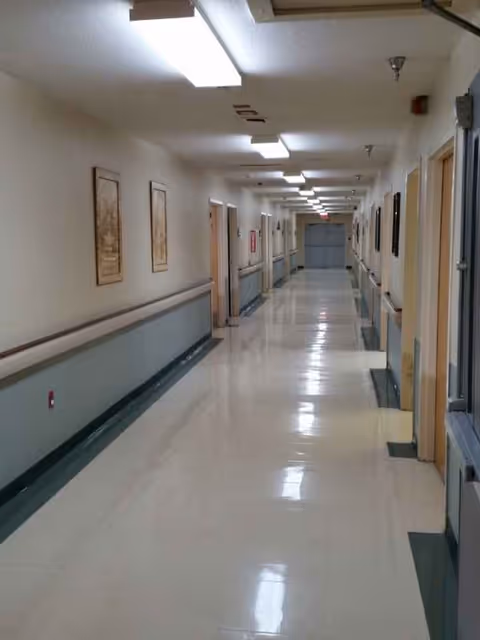 Long bright hallway inside a senior living center with doors and wall rails.