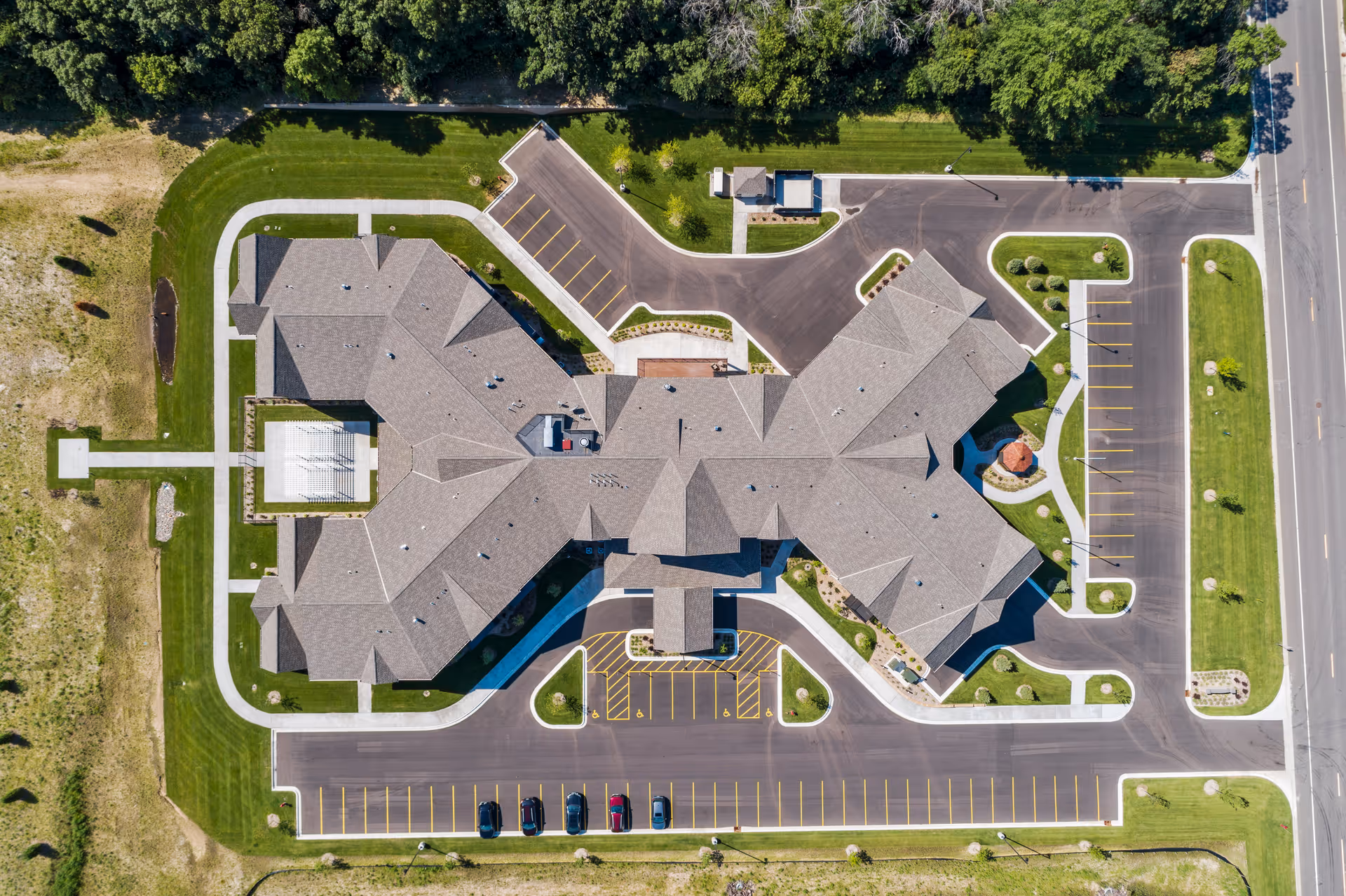 Aerial view of Cedar Creek Senior Living facility showing the building's roof, surrounding parking lots, driveways, and landscaped green areas with trees and grass.