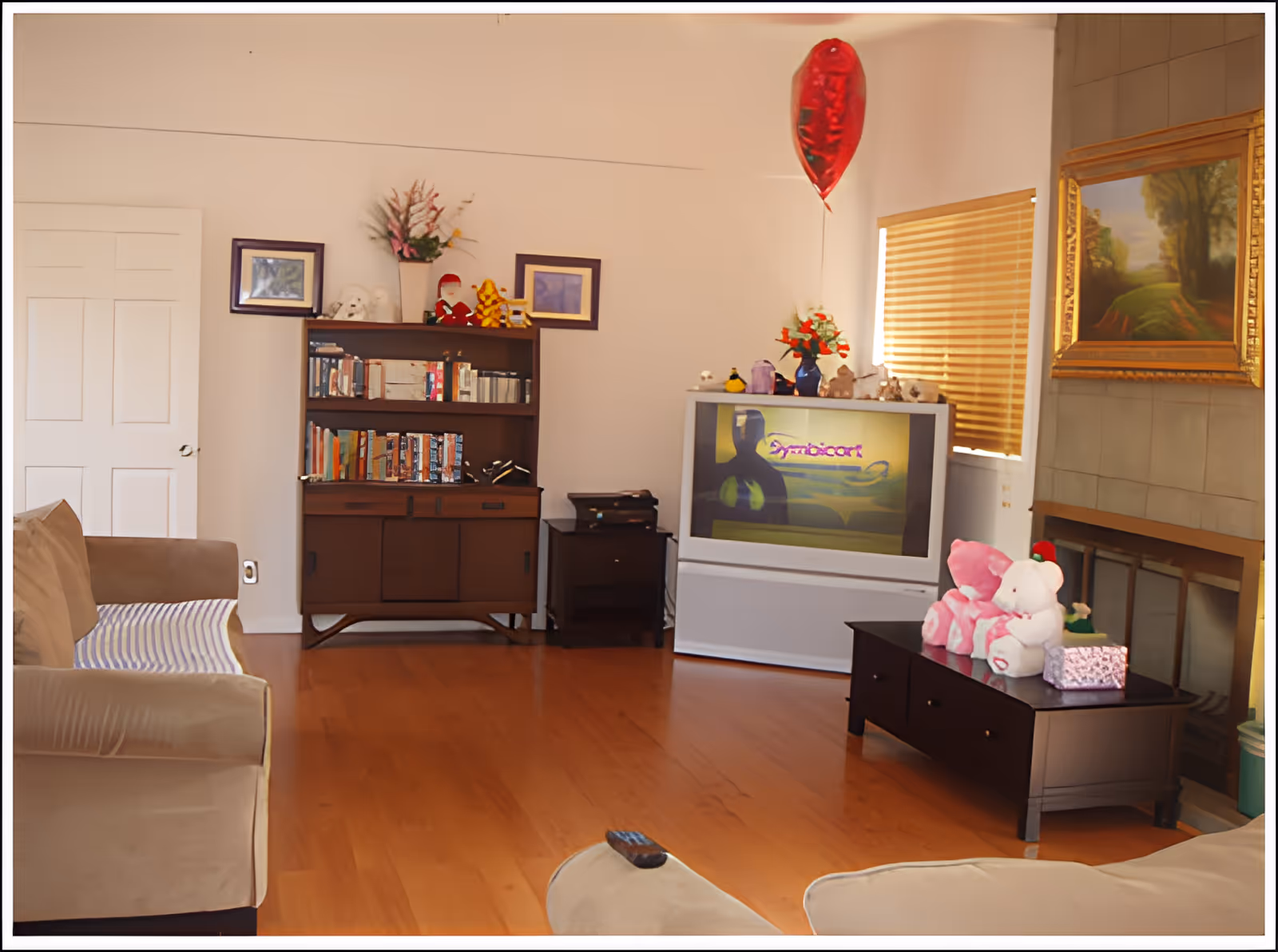 Cozy living room with sofas, a bookshelf, a TV, and a coffee table topped with stuffed animals and a red balloon.