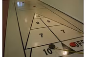 Indoor shuffleboard court painted on a glossy floor with numbered scoring zones and two pucks (red and black).
