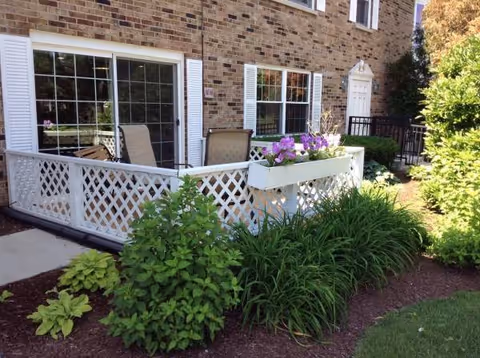 Brick building with a white lattice porch and outdoor seating surrounded by flowering planters.