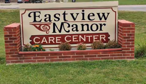 A brick sign reading Eastview Manor Care Center sits beside a small flower bed.