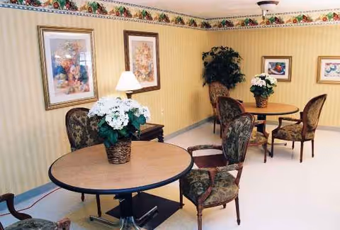 Cozy indoor lounge with round tables, upholstered chairs, lamps, and potted plants.