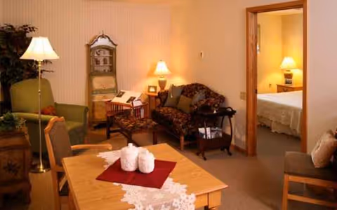 Cozy senior living common area with a dining table, seating, and an adjacent bedroom doorway.