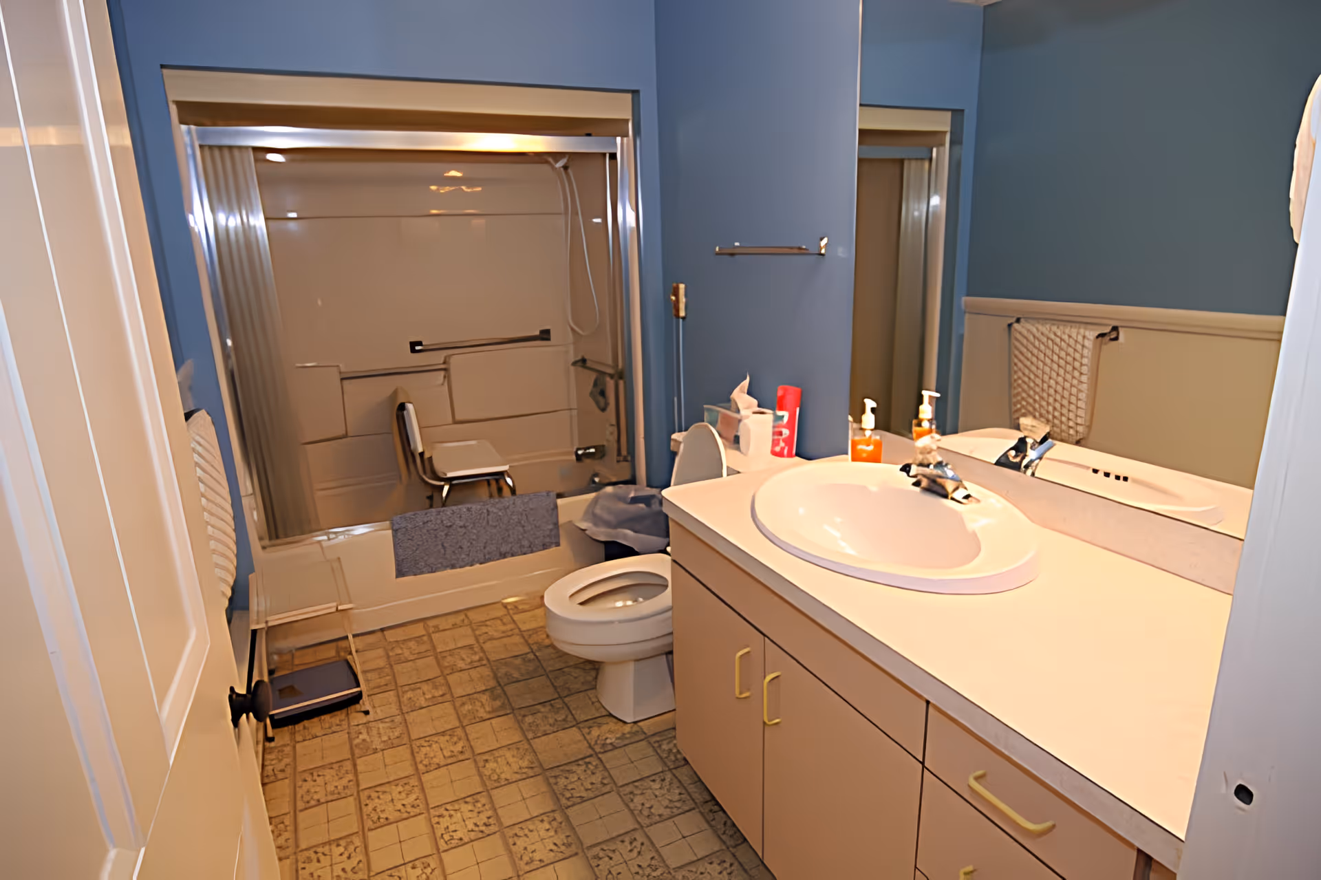 A bathroom with a sink and vanity, toilet, and bathtub equipped with a shower chair and grab bars.